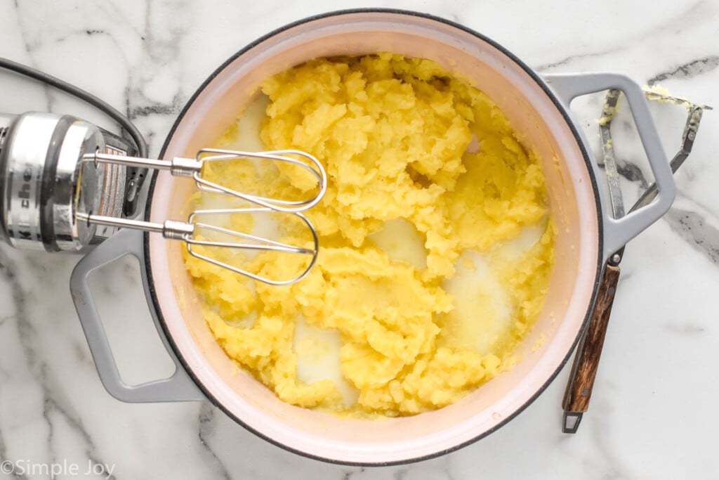 Overhead pot of mashed potatoes ingredients with hand mixer and potato masher sitting beside
