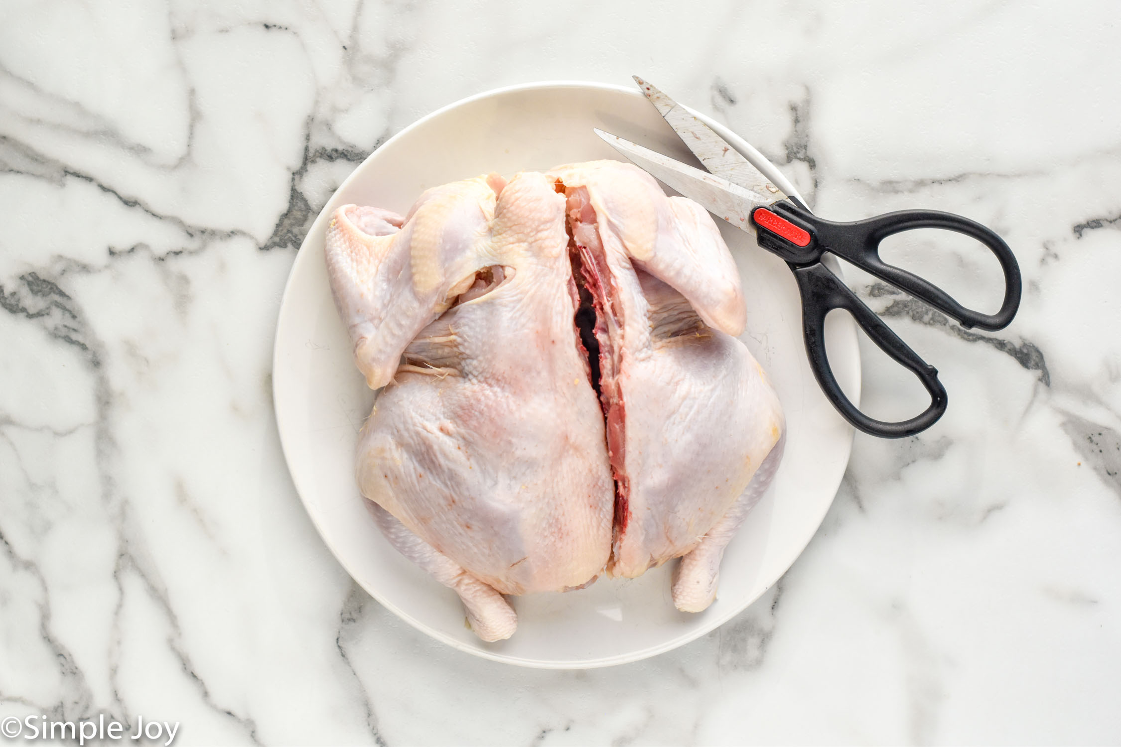 Overhead of raw chicken cut open to make spatchcock chicken with kitchen shears sitting beside