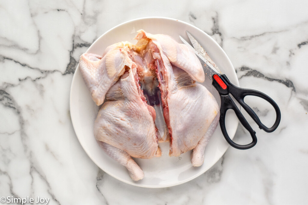 Overhead of raw chicken cut open to make spatchcock chicken with kitchen shears sitting beside