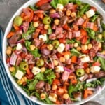Overhead photo of Italian Chopped Salad in a white bowl with whole tomatoes, a wooden serving spoon, and dressing in the background - 9