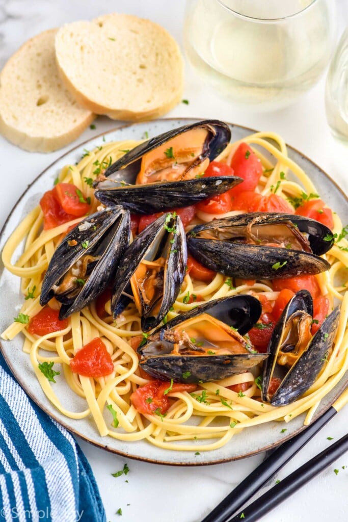 plate of pasta topped with tomatoes and served with mussels recipe with two slices of bread and glass of wine sitting in background