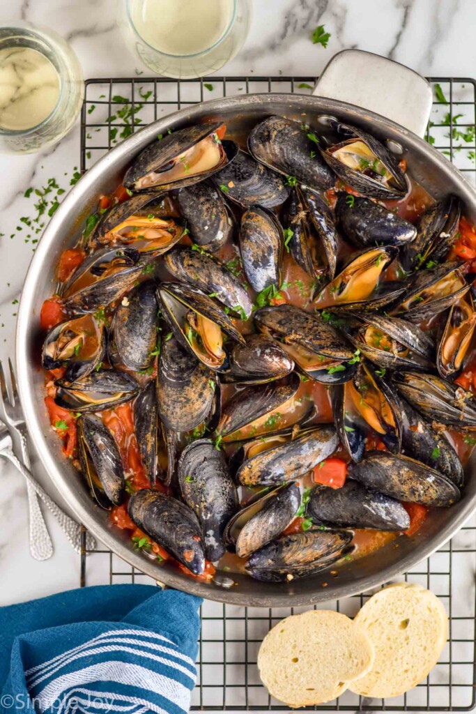 overhead of pan of cooked mussels ready for serving with two slices of bread and two glasses of white wine sitting beside
