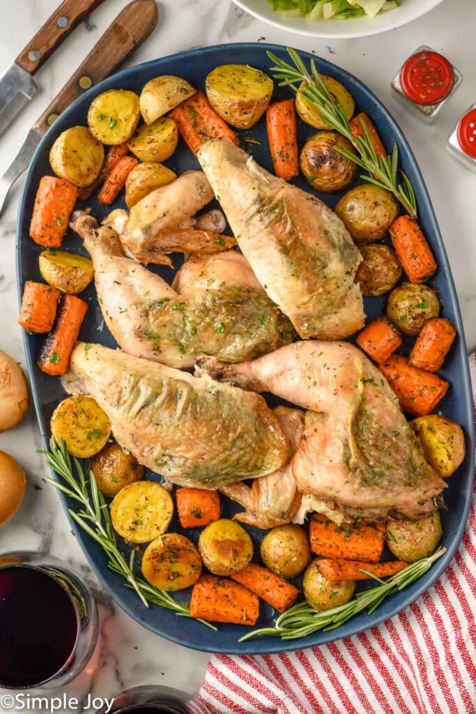 overhead of serving platter of carved spatchcock chicken, carrots, and potatoes garnished with rosemary