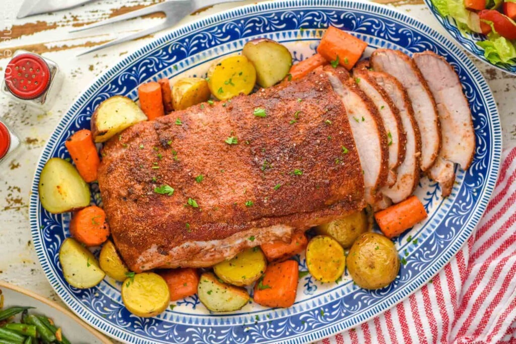 overhead of pork roast surrounded by potatoes and carrots for serving