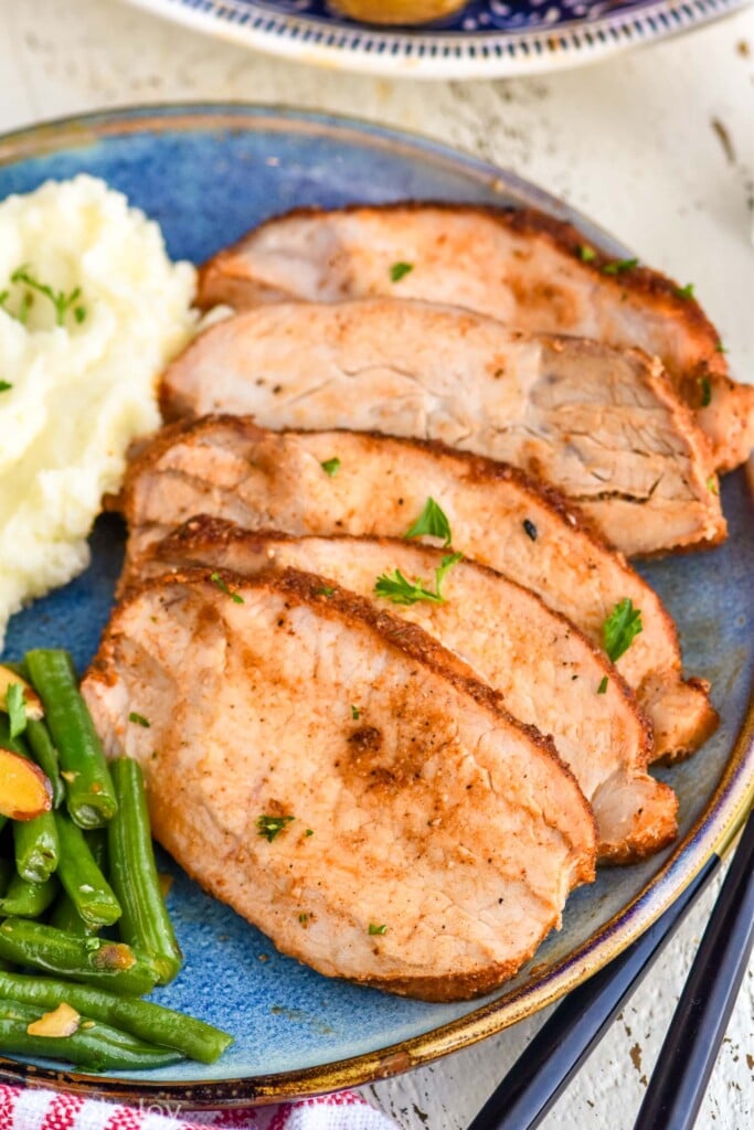 sliced pork roast on a plate with green beans almondine and mashed potatoes