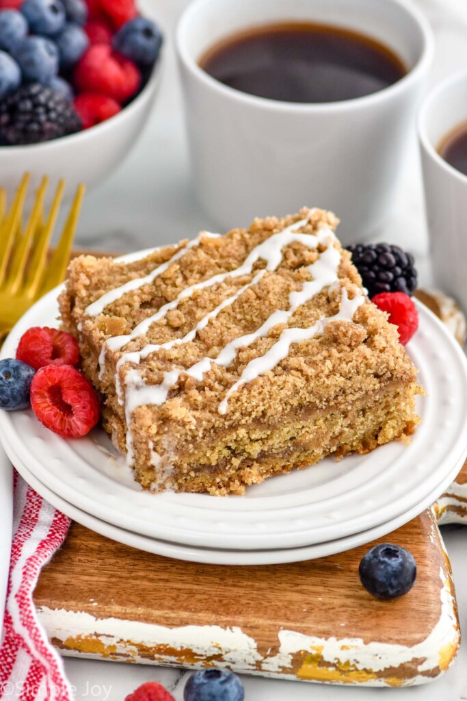 plate of coffee cake with fresh fruit, bowl of fruit and mug of coffee sitting in background