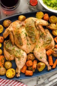 Overhead of serving platter of spatchcock chicken, potatoes, and carrots for serving.