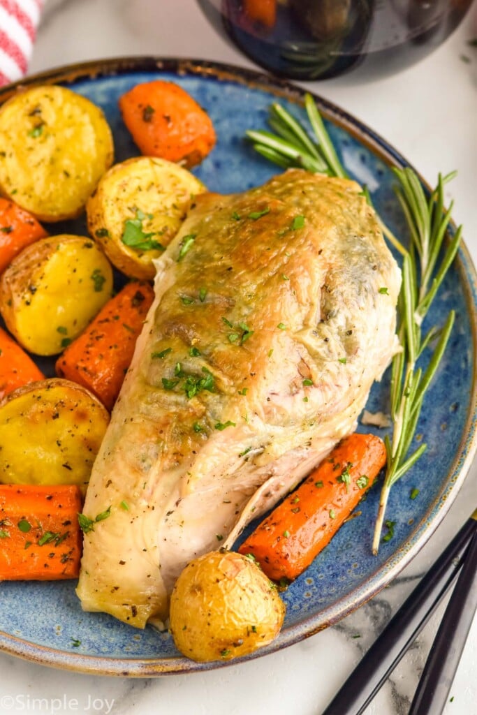 dinner plate of spatchcock chicken, potatoes, and carrots garnished with rosemary for serving.