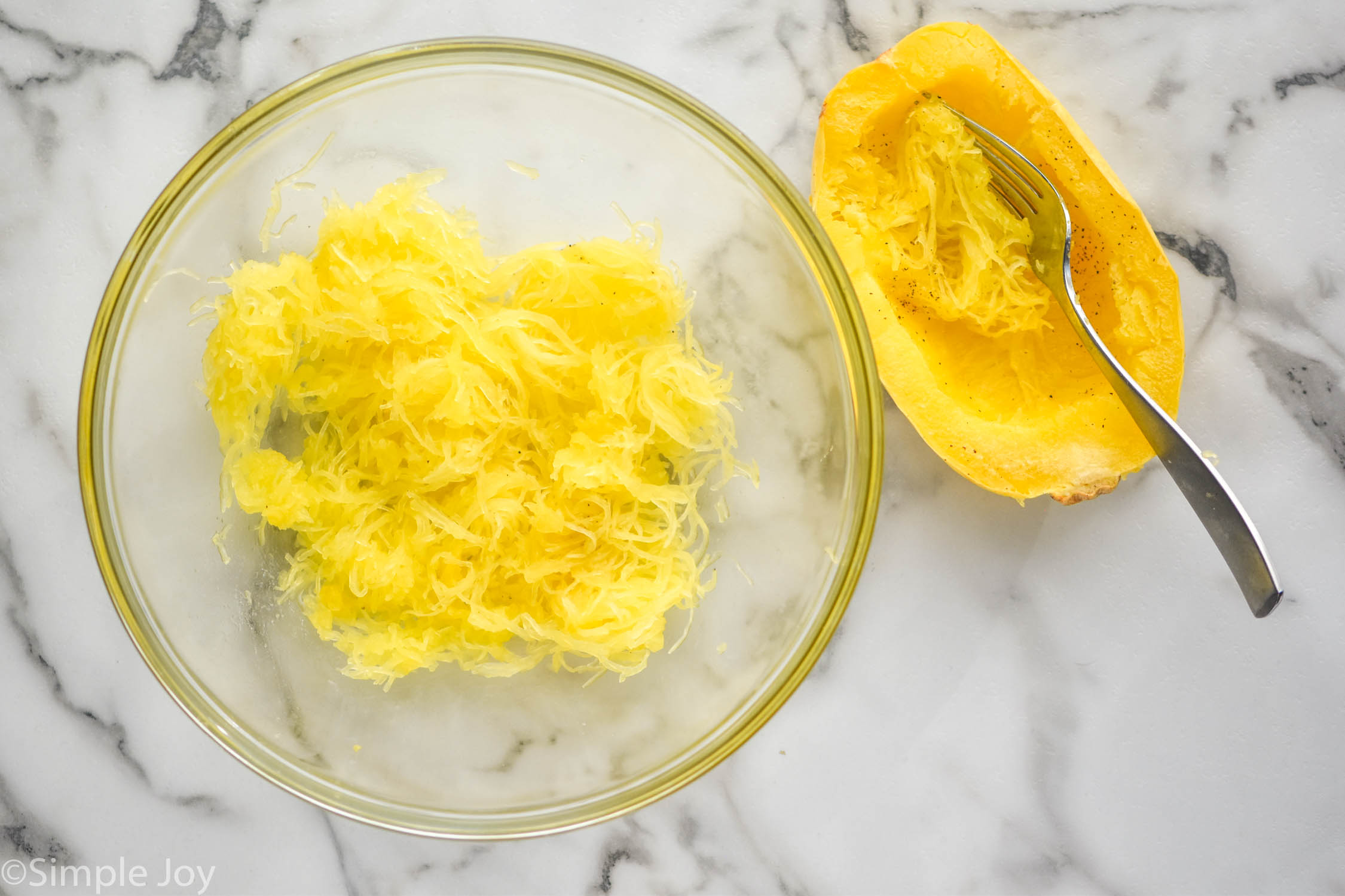 Overhead photo of a bowl of shredded spaghetti squash, with the spaghetti squash and a fork sitting beside bowl for Spaghetti Squash Casserole