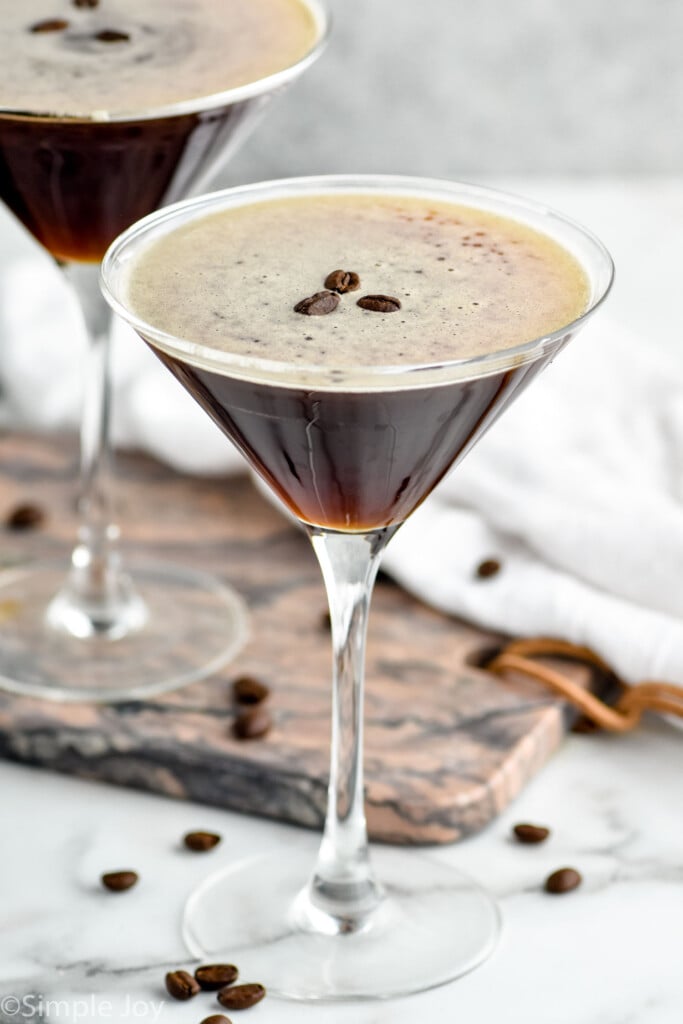 two martini glasses of espresso martinis garnished with coffee beans with coffee beans surrounding