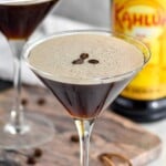 Pinterest graphic of espresso martini. Text says "the best espresso martini simplejoy.com" Image shows a martini glass of espresso martini topped with coffee beans with bottle of Kahlua in the background