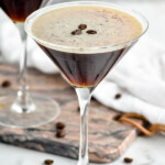 two martini glasses of espresso martinis garnished with coffee beans with coffee beans surrounding - 9