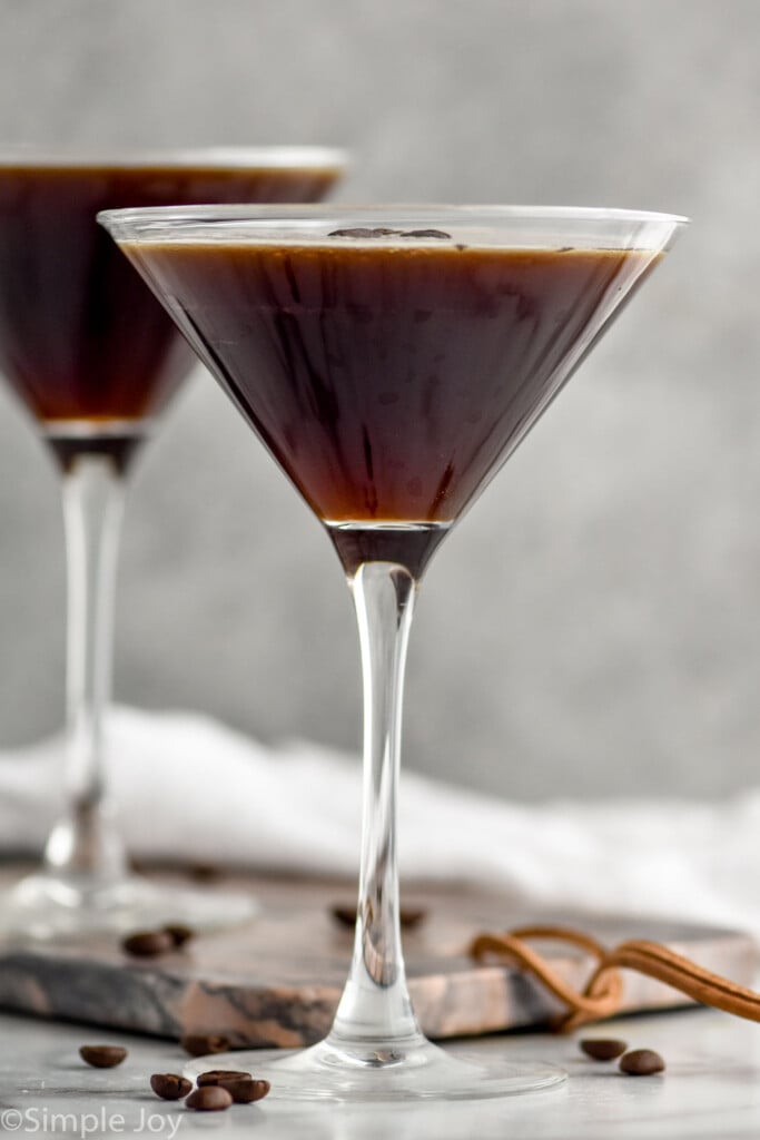 two martini glasses of espresso martinis garnished with coffee beans with coffee beans surrounding