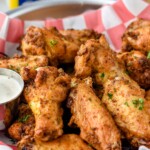 Close up photo of Old Bay Chicken Wings served with homemade ranch dressing for dipping,. Container of Old Bay Seasoning in the background.