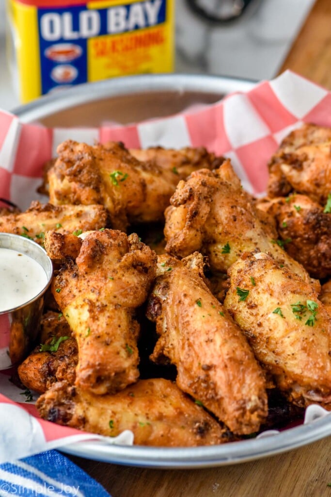 Close up photo of Old Bay Chicken Wings served with homemade ranch dressing for dipping,. Container of Old Bay Seasoning in the background.