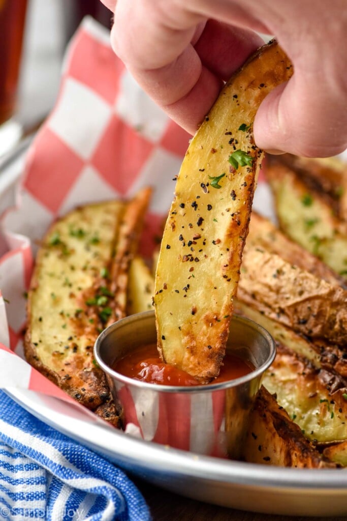 Close up photo of person's hand dipping Air Fryer Potato Wedge into ketchup.