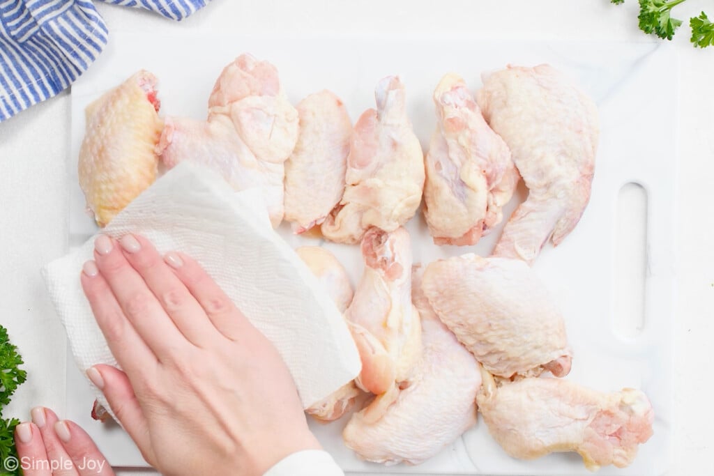 a hand patting chicken wings dry with a paper towel
