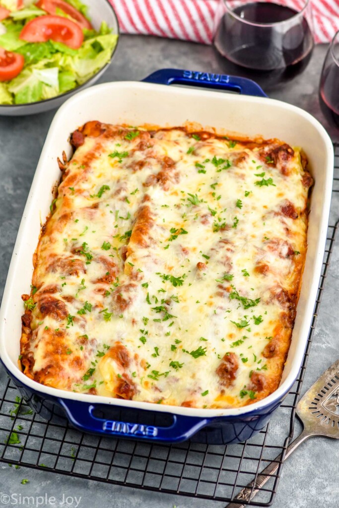 Overhead photo of a baking dish of Homemade Lasagna. Side salad and glass of wine are on counter beside lasagna.