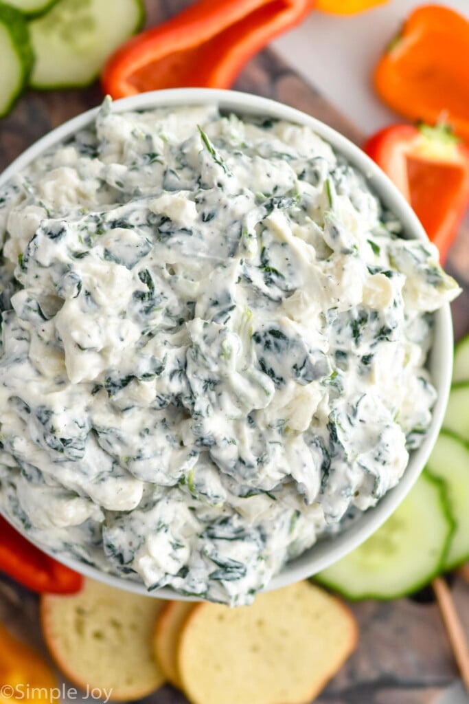 Overhead photo of Spinach Dip Recipe served in a bowl. Sliced peppers, cucumbers, and chips beside bowl for dipping.