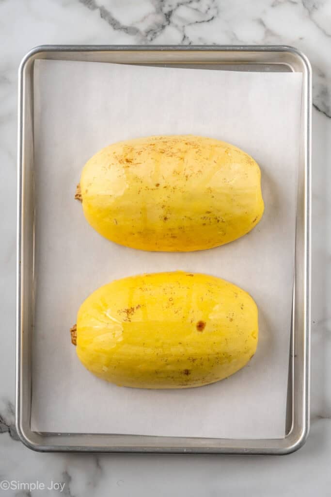 overhead of a spaghetti squash on a rimmed baking sheet lined with parchment paper cut in half, with the cut side down