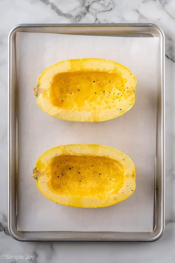 overhead of a spaghetti squash on a rimmed baking sheet lined with parchment paper cut in half, seeds and pulp removed, and seasoned with olive oil, salt, and pepper