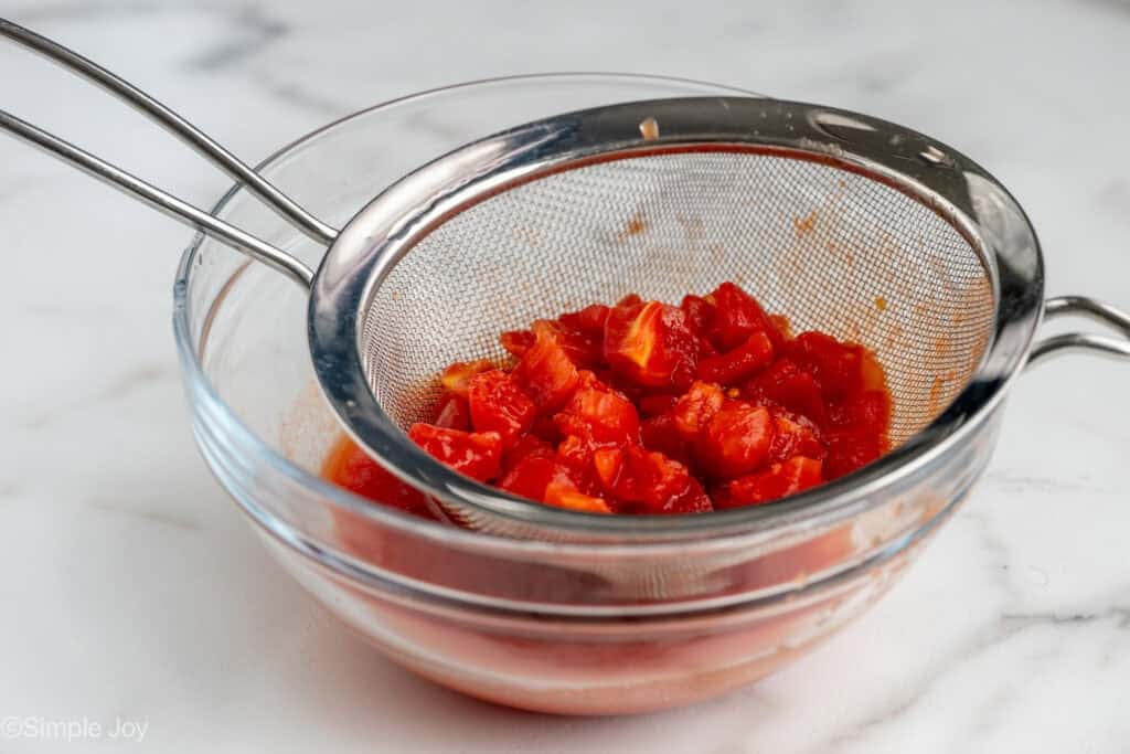 diced tomatoes in a metal sieve over a glass bowl