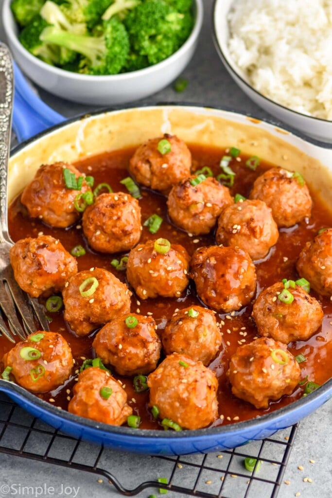 Overhead photo of a pan of Teriyaki Meatballs. Bowls of rice and broccoli sit beside pan.