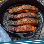 Pinterest graphic for Blackened Salmon recipe. Image is overhead photo of Blackened Salmon in a skillet with bowls of salad and rice beside skillet. Text says, "25 minute Blackened Salmon simplejoy.com."