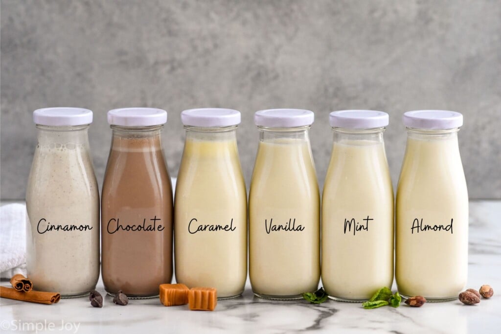 Photo of a row of jars of Homemade Coffee Creamers. Jars say, "cinnamon, chocolate, caramel, vanilla, mint, almond."