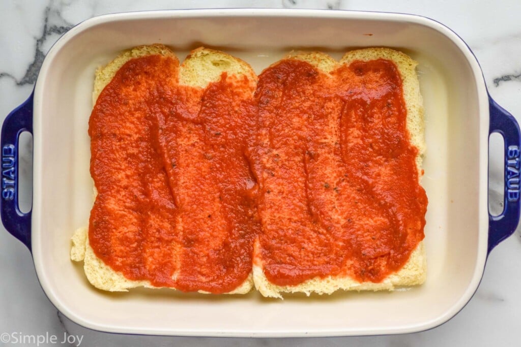 Overhead photo of a baking dish with dinner rolls and sauce for Pizza Sliders recipe.