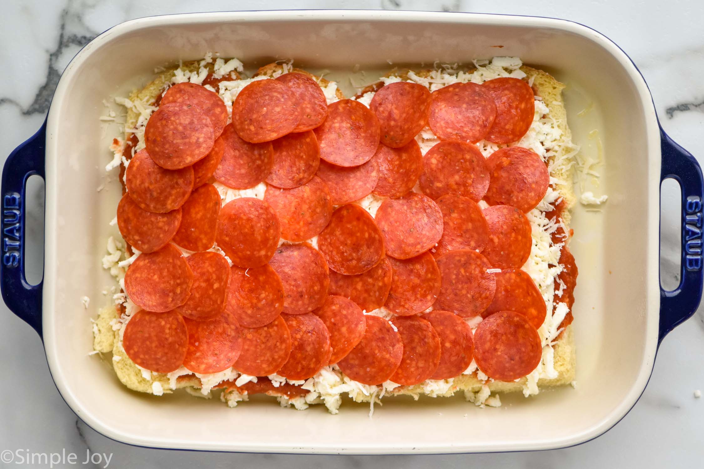 Overhead photo of ingredients layered in baking dish with pepperoni on top for Pizza Sliders recipe.