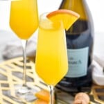 Pinterest graphic for Mimosa recipe. Text says, "the best Mimosa recipe simplejoy.com." Image is overhead photo of Mimosa garnished with orange wedge. Bottle of champagne and another mimosa in the background.