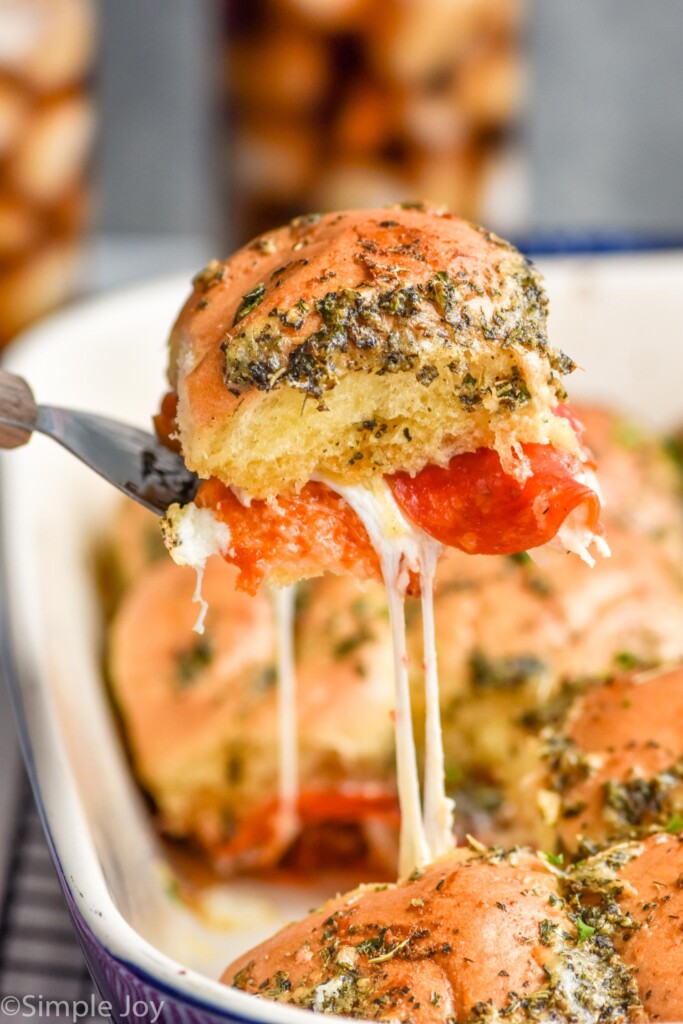 Close up photo of a piece of Pizza Sliders recipe being lifted out of baking dish of Pizza Sliders.