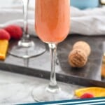 Pinterest graphic for Raspberry Mimosa recipe. Photo of Raspberry Mimosas garnished with orange slices. Bottle of prosecco wine in background. Orange slices and raspberries on counter beside flutes. Text says, "Raspberry Mimosa simplejoy.com"