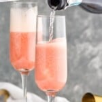 Pinterest graphic for raspberry mimosa recipe. Text says, "amazing raspberry mimosa simplejoy.com." Image is photo of bottle of sparkling wine being poured into flutes of juice for raspberry mimosa recipe.