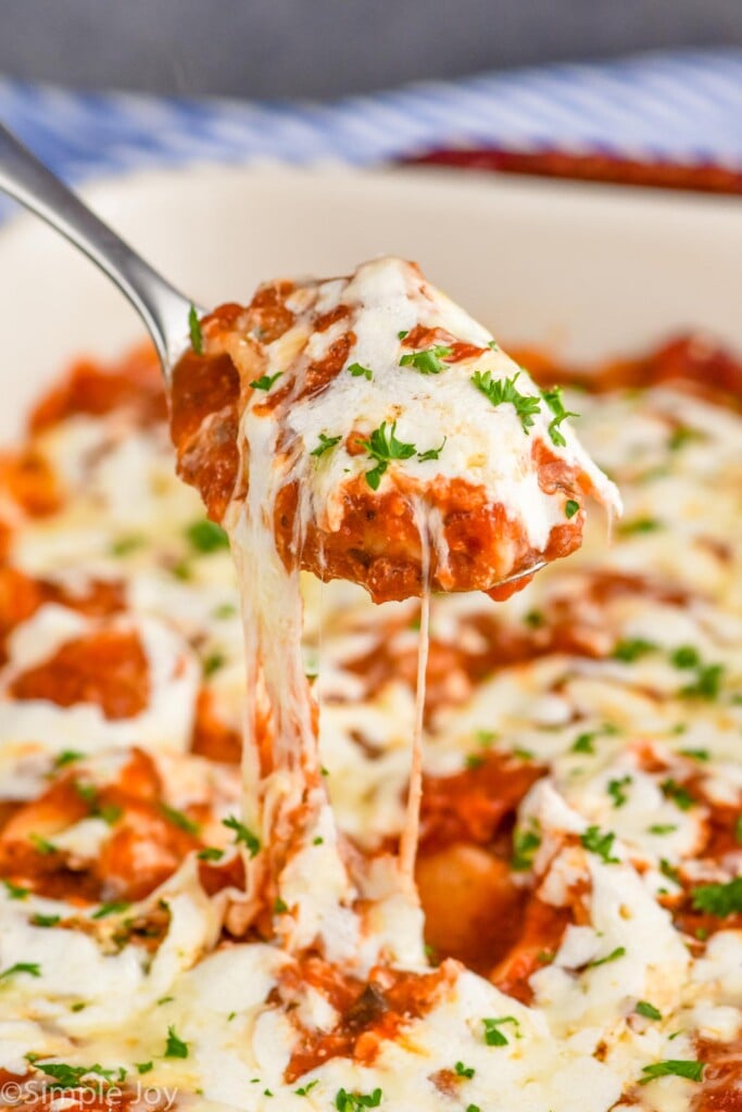 Photo of a spoon pulling a bite of Stuffed Shells out of baking dish of Stuffed Shells recipe.