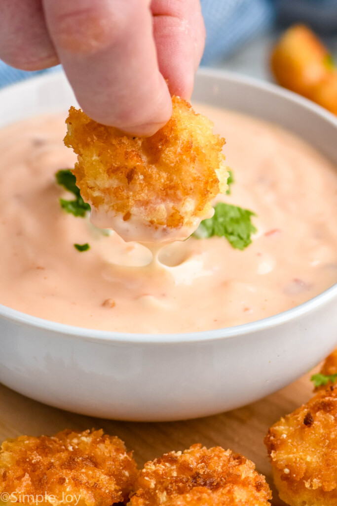 Close up photo of person's hand dipping breaded shrimp into bowl of Bang Bang Sauce