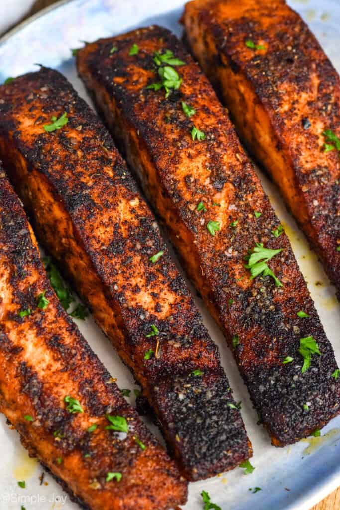 four pieces of blackened salmon on a plate, garnished with parsley