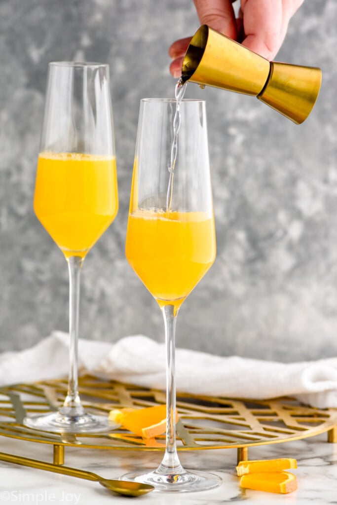 Photo of person's hand pouring ingredients into flute glass for mimosa recipe.
