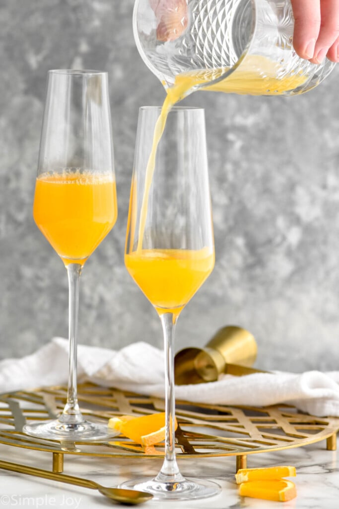 Photo of person's hand pouring orange juice into flute glasses for mimosa recipe.