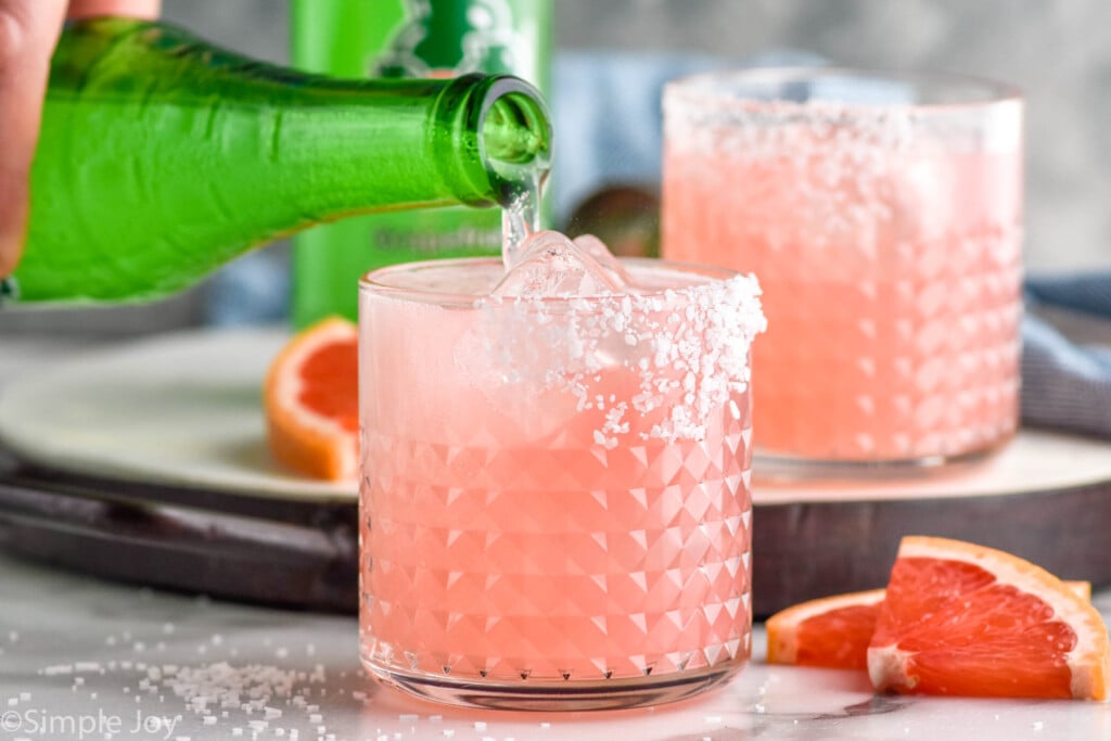 Photo of grapefruit soda being poured into glass of ingredients for Paloma recipe.