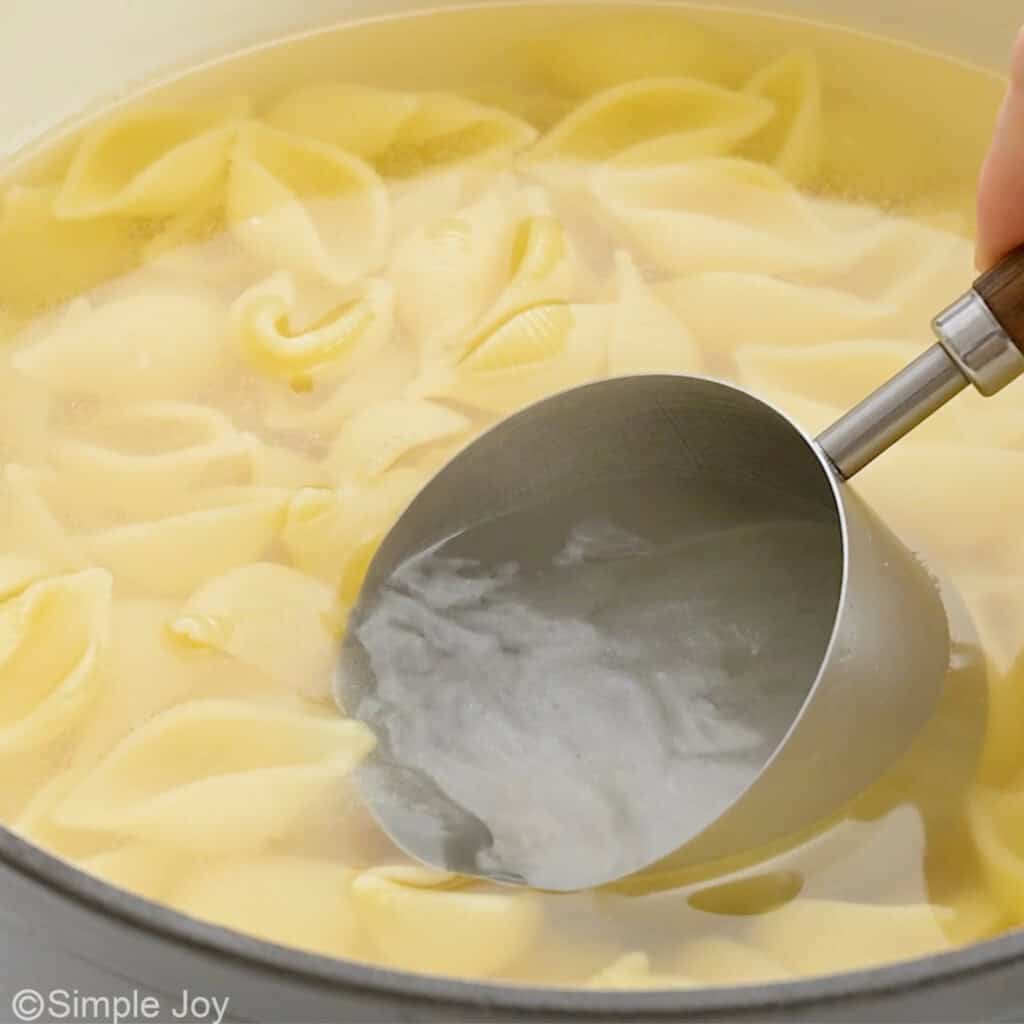 a measuring cup pulling pasta water out of a pot