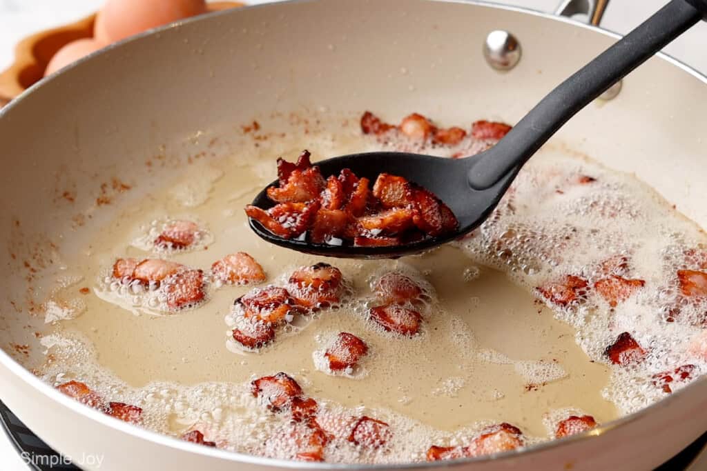 a slotted spoon pulling cooked bacon pieces out of a frying pan