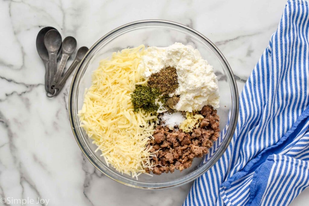 Overhead photo of a mixing bowl of ingredients for Stuffed Shells recipe. Measuring spoons sit beside bowl.