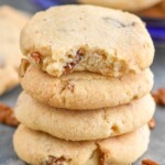 Close up photo of a stack of Pecan Sandies with a bite missing out of the top cookie. Pecans on counter beside stack of Pecan Sandies. - 8