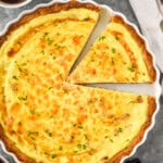 overhead of quiche Lorraine with one slice cut and ready to come out