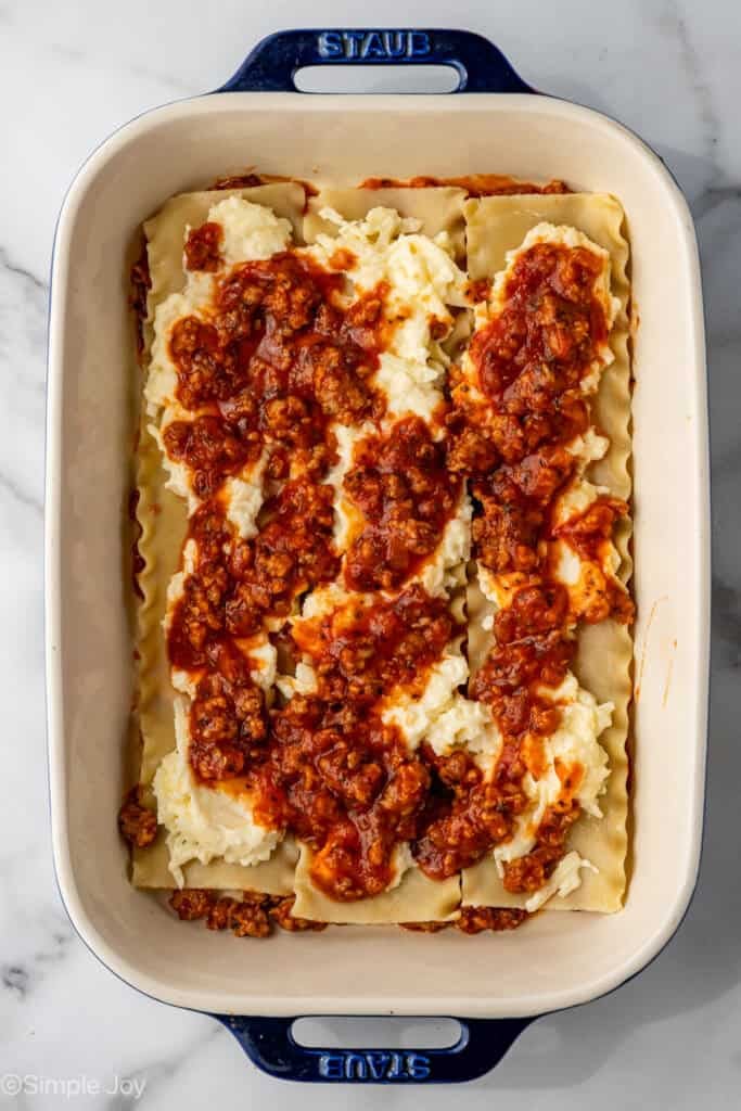 overhead of a lasagna being put together with noodles, a cheese layer, and a meat sauce layer