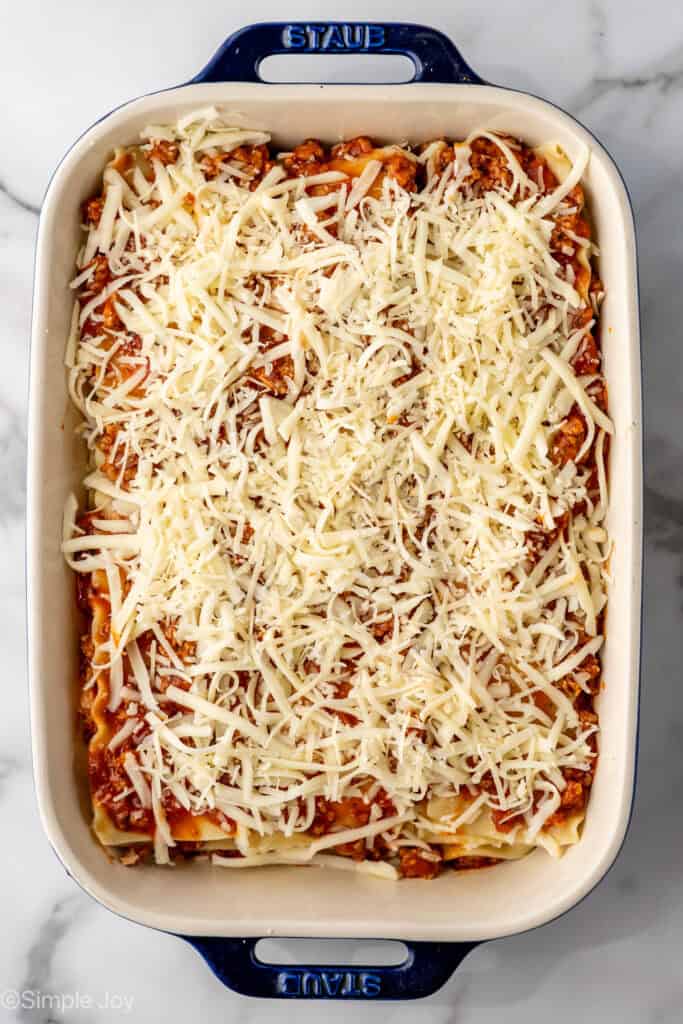 an unbaked lasagna with a mixture of mozzarella and parmesan cheese on top