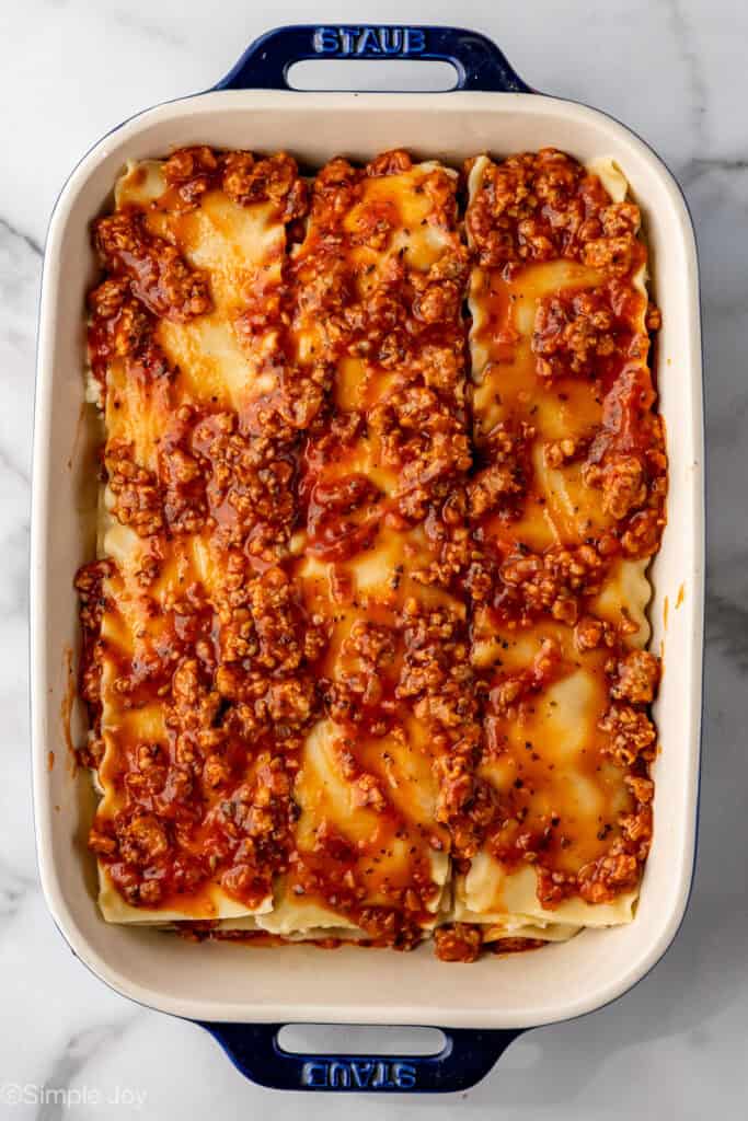 an unbaked lasagna topped with meat sauce