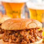 Pinterest graphic for Homemade Sloppy Joes recipe. Text says, "Amazing sloppy joe recipes simplejoy.com." Image is close up photo of Homemade Sloppy Joes sandwiches with glasses of beer in the background.
